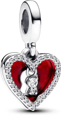 A close-up studio shot of a silver heart-shaped charm with red enamel and clear stones, featuring a keyhole design.