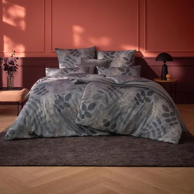 A bedroom scene with a bed dressed in a leaf-patterned duvet cover.