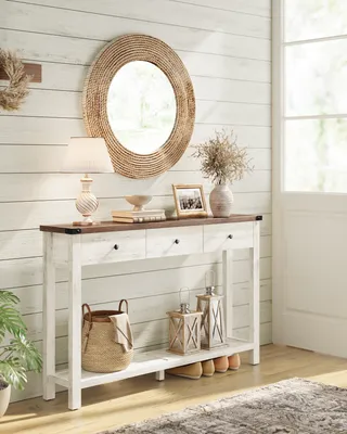 A console table with drawers and a shelf, decorated with a lamp, books, a framed photo, a vase with dried flowers, a basket, lanterns, and shoes.
