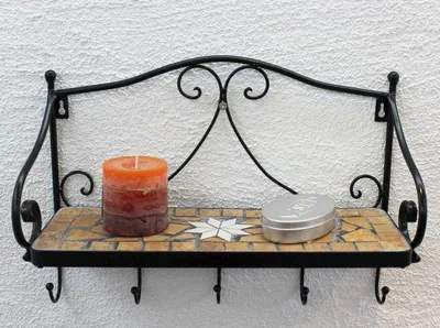 A black metal shelf with mosaic tile surface, holding a candle and a silver tin.