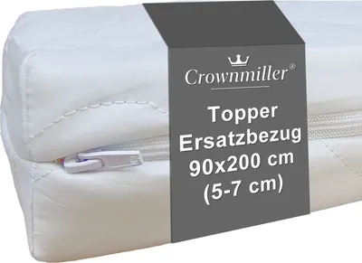 A close-up of a white topper mattress cover with a gray band containing product information.
