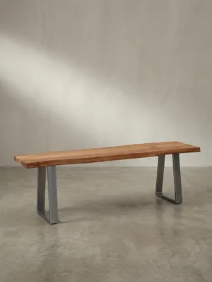 Schräge 3/4-Ansicht der 120x40 cm großen Massivholzbank, die die Tiefe der Sitzfläche aus Akazie und die glänzenden Metallkufen hervorhebt._#sku_SAFWL7.293#