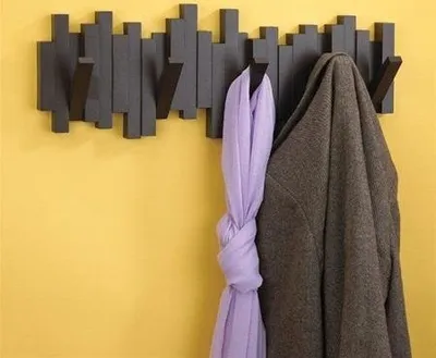 A coat and scarf hanging on a modern coat rack mounted on a yellow wall.