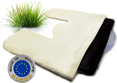 A cream-colored cushion with a black insert, placed on a white surface with a tuft of grass in the background. A circular 'Made in Europe' badge is visible in the lower left corner.
