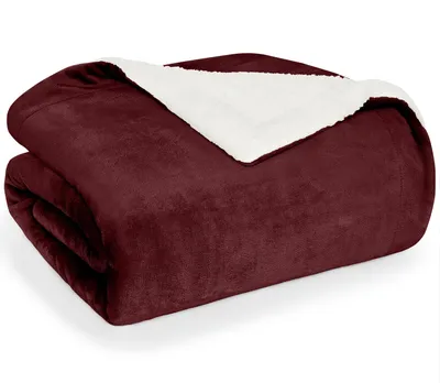 A folded dark red blanket with a white sherpa lining is shown against a white background.