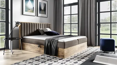 A bedroom scene featuring a large boxspring bed, bedside table, and large windows.