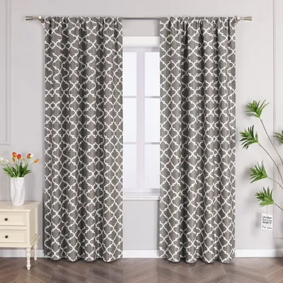 A pair of gray curtains with a white geometric pattern hang on a curtain rod in front of a window. A small bedside table with a vase of tulips is to the left, and a plant is to the right.