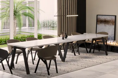 A modern dining room with a long white table and chairs, set in front of large windows overlooking a garden.