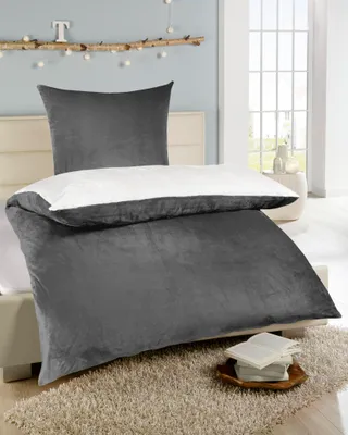 A bed with dark gray bedding and a white pillow, set in a bedroom with decorative branches and lights on the wall.
