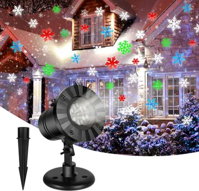 A snowflake projector light is shown projecting colorful snowflakes onto a house and trees decorated for winter.