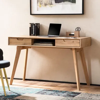 A wooden desk with a laptop, books, and office supplies, placed in a room with a chair and a rug.