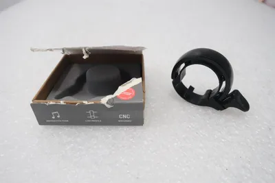 A bicycle bell and its packaging are displayed on a textured white surface.