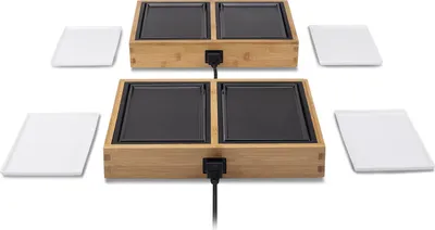 Two tabletop grills with bamboo bases and black cooking surfaces, each with two square cooking plates, are shown. Four white square plates are placed around the grills.