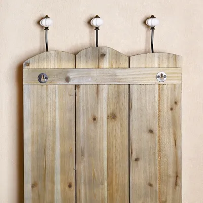Close-up of a rustic wooden coat rack with decorative ceramic knobs, mounted on a light-colored wall.