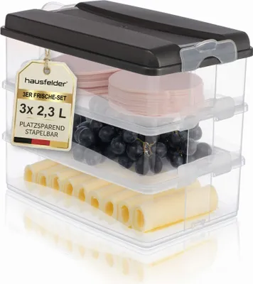 A set of three clear plastic food storage containers with dark grey lids, stacked and filled with food items.