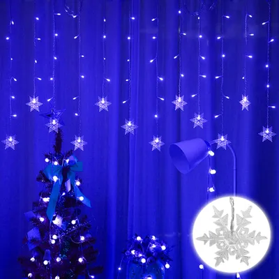 A decorated Christmas tree and a lamp are illuminated by blue snowflake string lights against a blue curtain background.