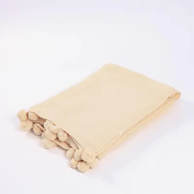 A folded beige blanket with pom-poms on a white background.