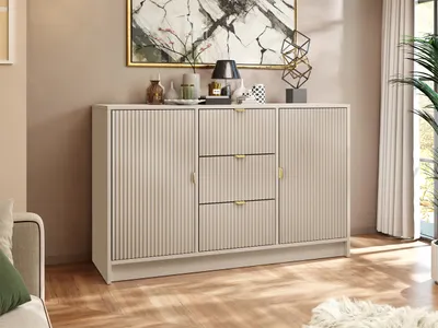 A sandbeige sideboard with fluted doors and drawers, decorated with a lamp, vases, and a sculpture, placed in a room with a painting on the wall and a plant in the background.