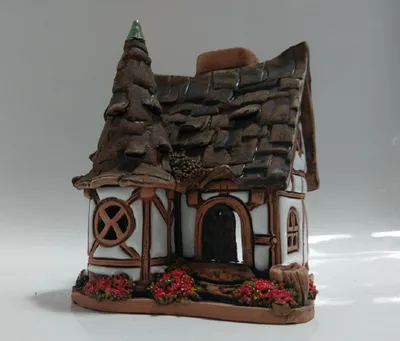 Das handgefertigte Haus ist detailreich gestaltet, mit einem dunkelbraunen, schieferartigen Dach.