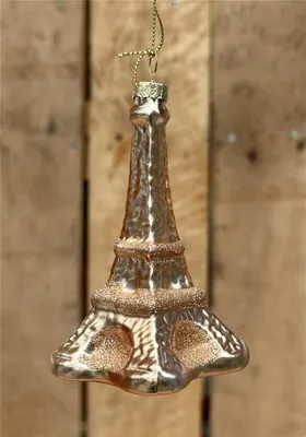 A glass Eiffel Tower ornament hangs against a wooden background.