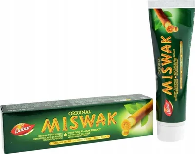A box of Dabur Miswak Herbal Toothpaste is shown in the foreground, with a tube of the same toothpaste positioned to the right and slightly behind it.