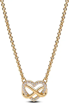 A close-up studio shot of a gold necklace with a heart-shaped pendant adorned with small clear stones and an infinity symbol.