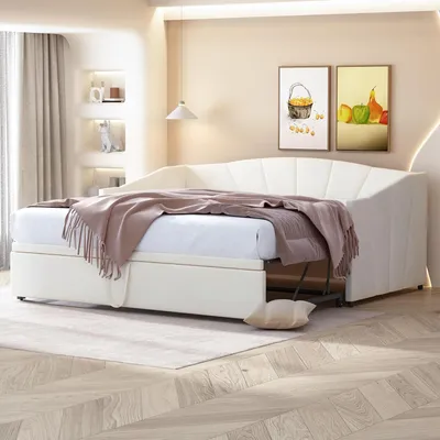 A beige upholstered daybed with a pull-out trundle bed is set up in a room with light beige walls and a wooden floor.