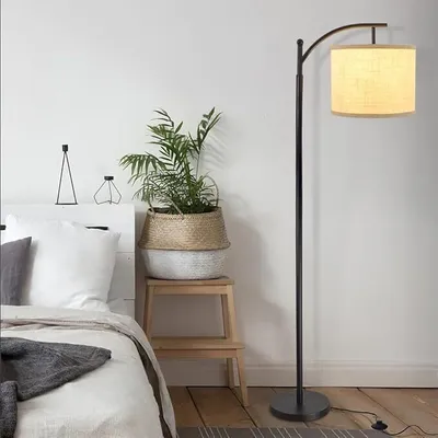 A bedroom scene with a bed, a plant, and a floor lamp.