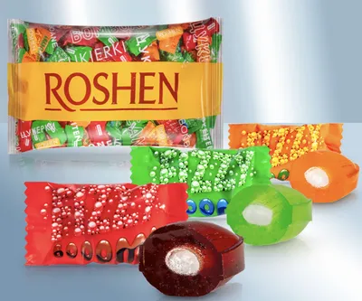 A collection of Roshen Fizzy Boom candies, some unwrapped and cut in half to show their filling, arranged on a light gray background.