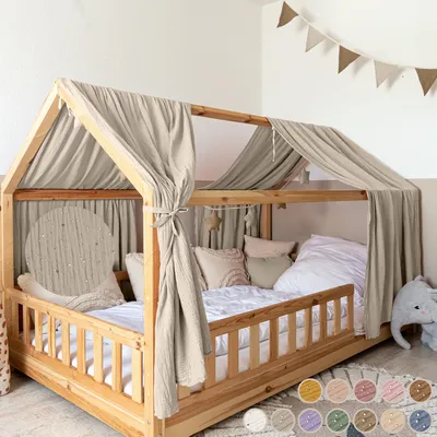 A child's house bed with a canopy and bedding, decorated with a garland.