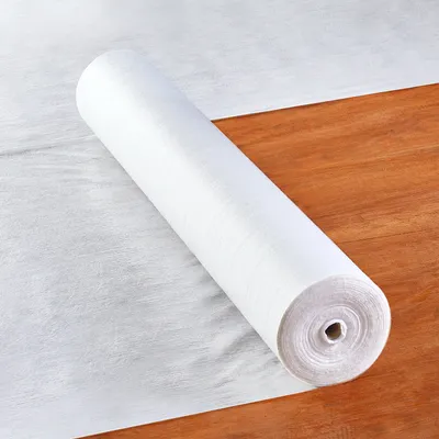 A roll of white fabric protection film is lying on a wooden floor.