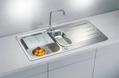 A stainless steel kitchen sink with a faucet, a cutting board, a drainer basket, and a bowl of oranges.
