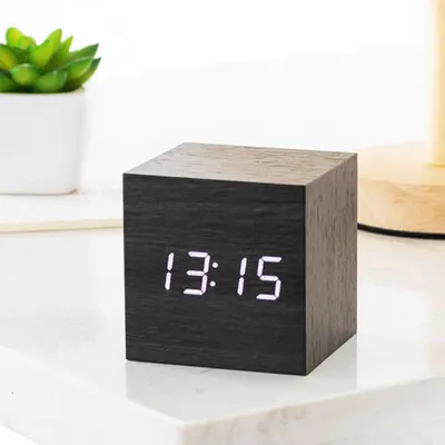 A black wooden cube alarm clock with a digital display showing the time.