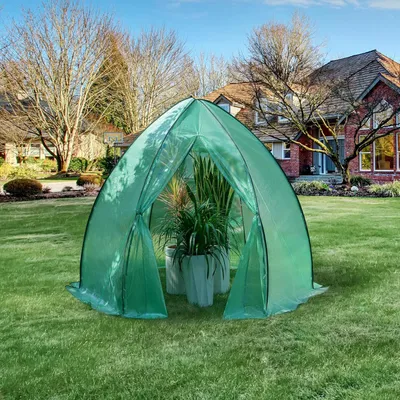 A green greenhouse tent is set up on a grassy lawn in front of a house.