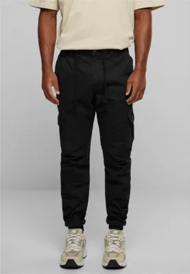 A man wearing black cargo jogging pants and beige sneakers, standing against a light gray background.