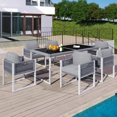 A patio dining set with chairs and a table is set up on a wooden deck next to a swimming pool.