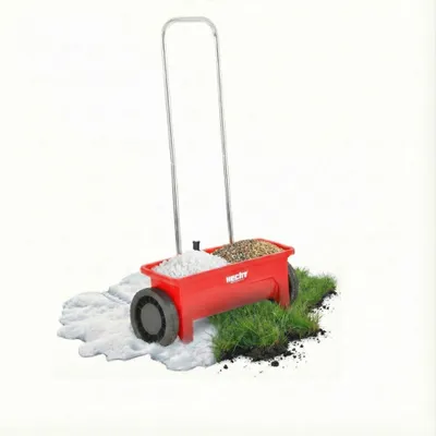 A red wheeled spreader filled with white granules and brown seeds, placed on a patch of grass and snow.