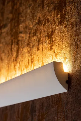 A close-up of a white decorative molding with integrated LED lighting, mounted on a textured brown wall.