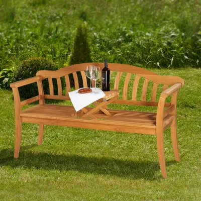 A wooden garden bench with a bottle of wine and two glasses on a small table attached to the bench, set in a grassy garden.
