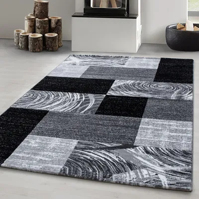 A modern abstract design rug with geometric patterns in black, gray, and white, placed on a light gray floor in a room with a fireplace and decorative logs.