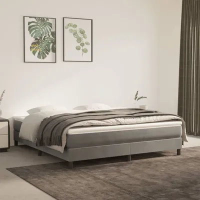 A bedroom scene featuring a grey boxspring bed with a mattress and bedding, two framed plant prints on the wall, and a rug on the floor.