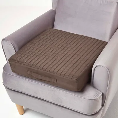 A brown seat cushion is placed on a gray armchair.