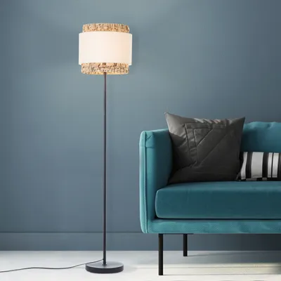 A floor lamp stands next to a teal sofa with pillows.