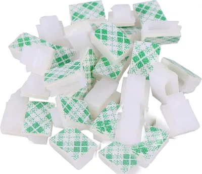 A pile of white cable clips with green adhesive backing.