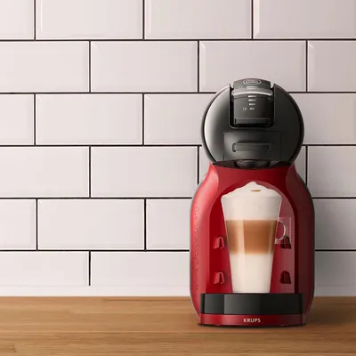 A red and black coffee machine is shown on a wooden counter in front of a white tiled wall.