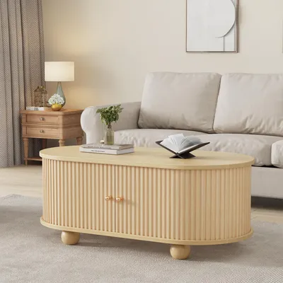 A modern oval coffee table with fluted detailing and gold knobs, placed on a light gray rug in front of a cream sofa.