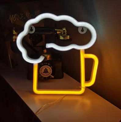 A neon sign shaped like a beer mug with foam is displayed on a shelf.