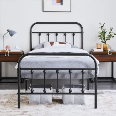 A black metal bed frame with bedding and storage baskets underneath, set in a bedroom.