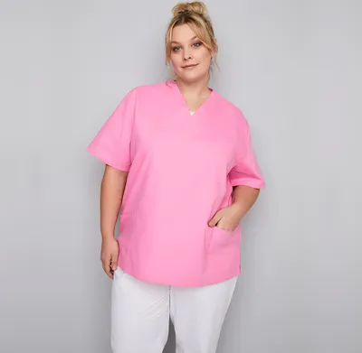 A woman wearing a pink scrub top and white pants against a gray background.