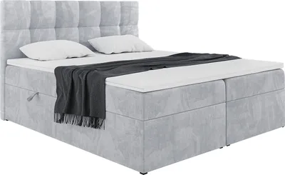 A light gray upholstered box spring bed with a headboard, two pillows, and a dark gray throw blanket.